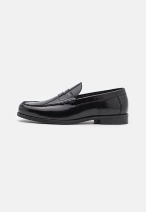 Mocassin penny pour homme en cuir noir, à talon bas et finitions cousues, sur un fond blanc uni.