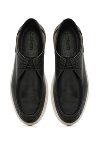 Chaussures noires en cuir avec une surface lisse, des coutures minimales et un bout rond. Présentent un accent en cuir marron contrastant et une semelle blanche.