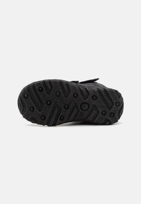 Semelle de chaussure en caoutchouc noir avec une surface texturée comportant des motifs circulaires et linéaires, conçue pour l'adhérence et la durabilité.