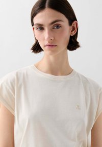 T-shirt in cotone color crema con maniche corte, dotato di scollo rotondo e un discreto logo ricamato sul petto. Tessuto liscio.