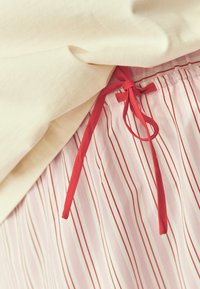 Gros plan d'un tissu rayé rose et blanc avec un cordon rouge noué en nœud sous un vêtement beige.