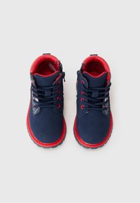 Bottes bleu marine avec des accents rouges, dotées de lacets, d'un col rembourré et d'une fermeture éclair latérale. Tissu texturé et semelle en caoutchouc avec un motif antidérapant.