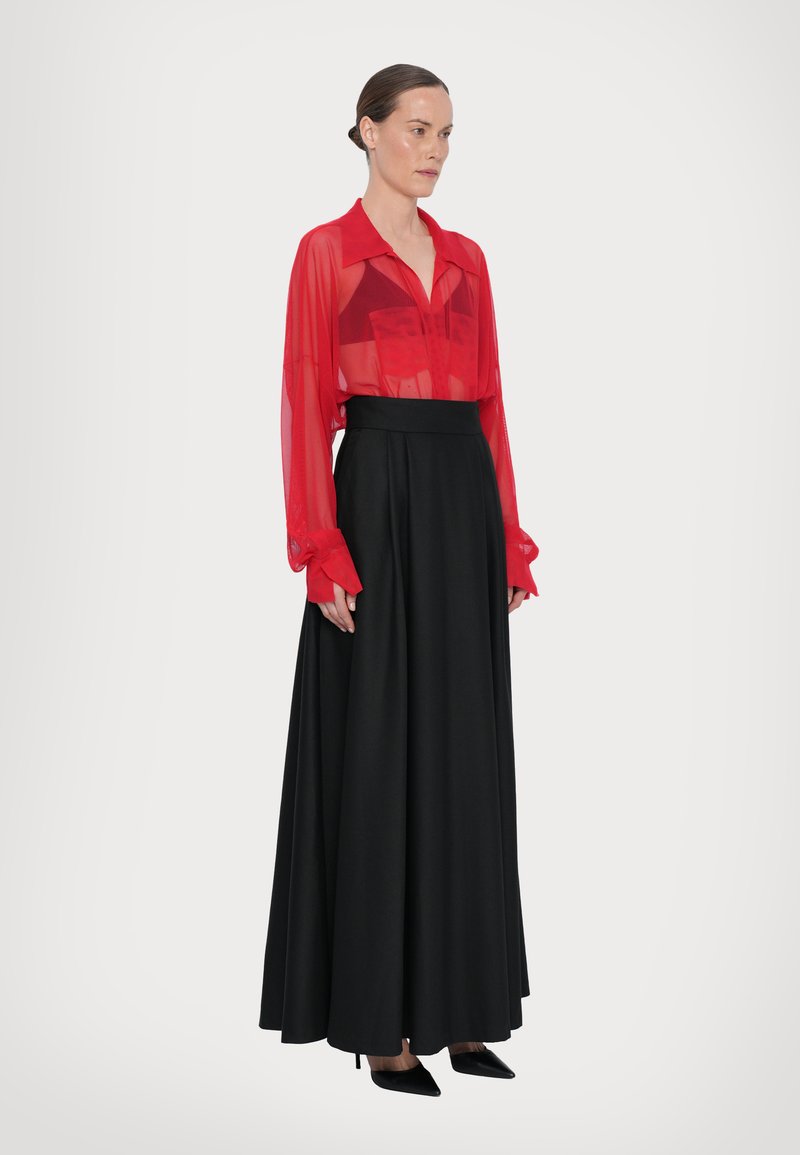 Blusa rossa trasparente con colletto e maniche lunghe, abbinata a una lunga gonna nera. Vestibilità slim, texture liscia. Tacchi a punta neri completano il look.