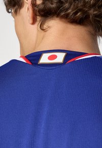 Person som bär en blå sporttröja med en japansk flaggpatch på baksidan av nacken och röda och vita kanter på kragen.