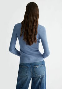 Ljusblå ribbad tröja med lång ärm, figursydd design och rundad sänka, kombinerad med högmidjade blå jeans, sedd bakifrån.