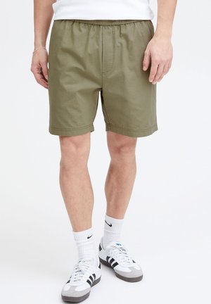 Olive green shorts with an elastic waist, a front pocket, and a loose fit. Worn with white socks and black-and-white athletic shoes.
