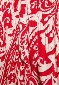 Tessuto rosso e crema con un grande motivo floreale e paisley, caratterizzato da una finitura testurizzata e un dettaglio in vita con elasticizzato arricciato.