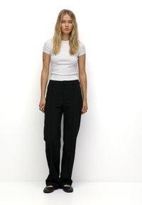 En åtsittande grå t-shirt och lösa svarta byxor. Byxorna har en slät textur och stängs med en knapp i fronten, styblade med svarta lägenheter.