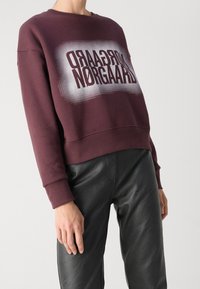 Sweat-shirt bordeaux avec impression graphique texturée, col rond et manches longues, associé à un pantalon en simili cuir noir.