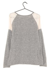 Chemise grise à manches longues avec des panneaux d'épaule en dentelle blanche, suspendue à un cintre en métal noir contre un fond blanc.