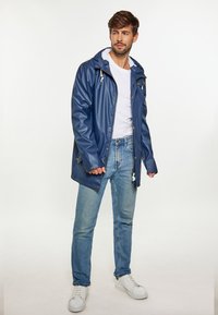 Marinblå vattentät jacka med huva, tryckknappar och dragsko. Kombinerad med ljusblå jeans och vita sneakers.