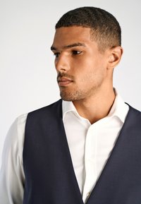 Marine-farbenes Weste mit glatter Textur über einem weißen Hemd, mit definiertem Kragen und Knopfverschluss, erzeugt einen formellen Outfit-Look.