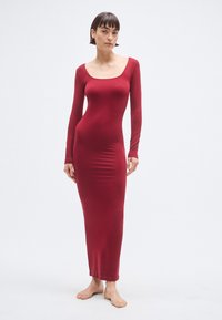 Červené priliehavé šaty s dlhým rukávom, štvorcovým výstrihom a dĺžkou do členkov, vyrobené z hladkej látky, ktorá zvýrazňuje kontúry tela.