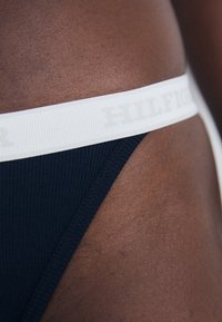 Mornarsko modri tangice z rebrasto teksturo in elastičnim belim pasom z diskretno natisnjenim logotipom "HILFIGER". Pogled od blizu na pas in tkanino.
