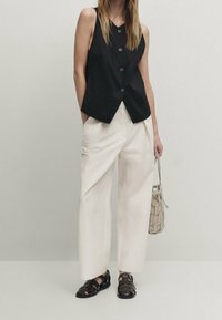 Black sleeveless top with button detail, light cream wide-leg trousers, and black strappy sandals. Beige woven handbag adds texture.