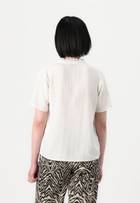 Crème korte mouw top met een gestructureerde afwerking en een gerimpelde halslijn, gecombineerd met beige broeken met een zwart zebra-streep patroon.