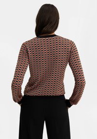 Kuvioitu neulepusero pitkillä hihoilla, jossa on aaltoileva kuvio punaisena, mustana ja valkoisena. Resorikaulus ja hihansuut sekä vartalonmyötäinen siluetti.