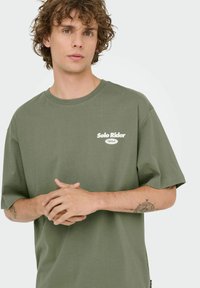 Olijfgroene katoenen T-shirt met korte mouwen, voorzien van een wit "Solo Rider" logo op de linkerborst. Zachte textuur en een ontspannen pasvorm.