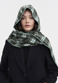 Écharpe à carreaux avec capuche dans des teintes de vert foncé et de menthe, présentant une finition texturée et un point de couture vert contrastant le long des bords.