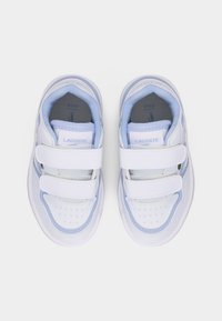 Ζεύγος παιδικών αθλητικών παπουτσιών Lacoste σε λευκό και ανοιχτό μπλε χρώμα, με διπλούς ιμάντες Velcro και μαξιλαρωμένα εσωτερικά πέλματα, φωτογραφημένα από πάνω σε λευκό φόντο.