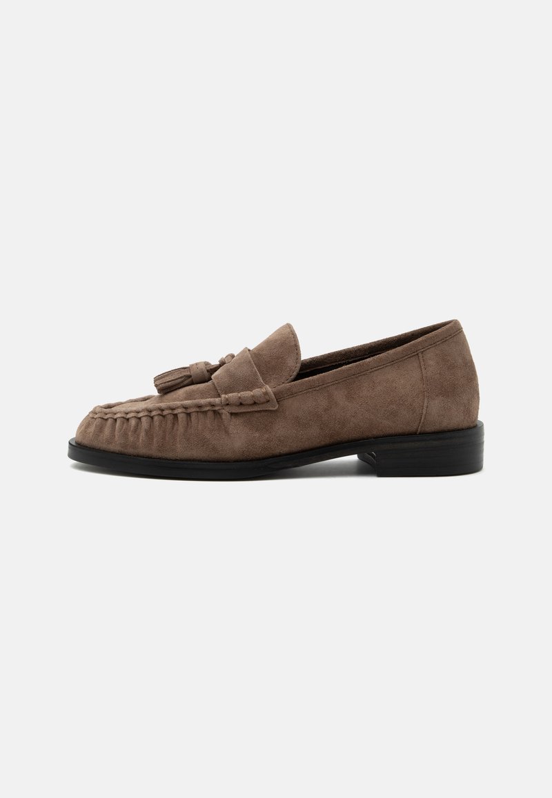 Mocassin en daim marron avec pompons, détails tressés et petit talon noir, présenté de profil sur fond blanc.