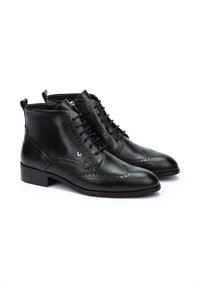 Botas negras de cuero hasta el tobillo con detalles de brogue, punta redonda y cierre de cordones. Tacón bajo y un sutil logo en el lateral.