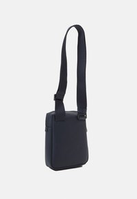 Borsa a tracolla blu navy realizzata in materiale testurizzato, con chiusura a zip e tracolla regolabile. Forma quadrata con design minimalista.