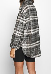 Flanellen overhemd in zwart, wit en grijs ruitpatroon. Beschikt over lange mouwen, een knoopsluiting bij de kraag en een zijsplit aan de onderkant. Zacht, textuur stof.