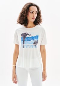 Valkoinen puuvillapaita, jossa on värikäs painettu kuvio palmupuista ja merimaisemasta sinisissä sävyissä. Lyhyet hihat ja pyöreä kaula-aukko.