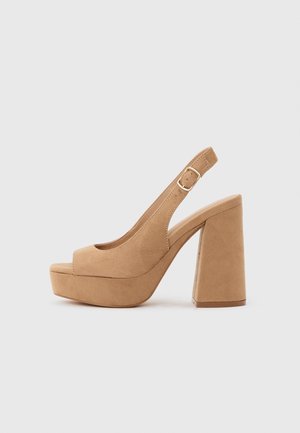 Beige ruskind platform højhælet sandal med åben tå og justerbar spænde på ensfarvet lys baggrund.
