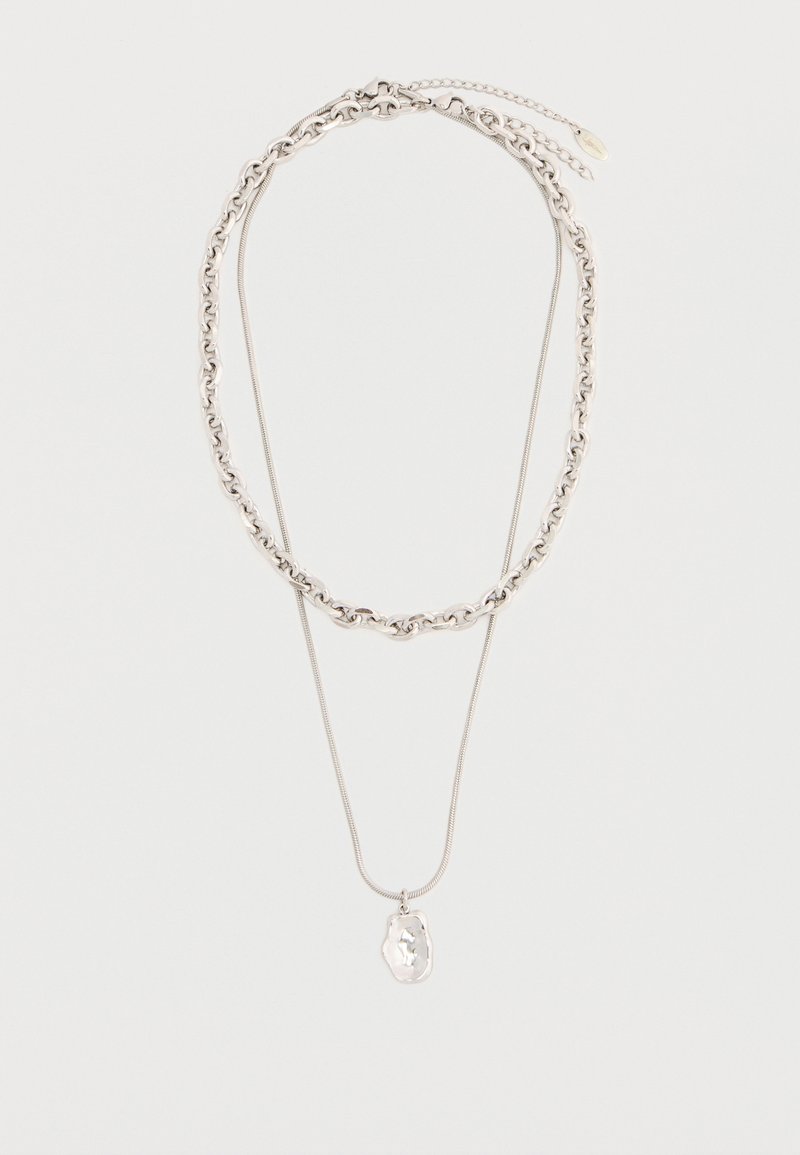 Δύο ασημένια κολιέ, ένα με χοντρή αλυσίδα και ένα με λεπτή αλυσίδα και ένα μενταγιόν ακανόνιστου σχήματος, τοποθετημένα επίπεδα σε λευκό φόντο.