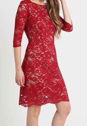 Punainen pitsimekko, jossa on kolme neljäsosaa hihat, kukkakuvio, vartalonmyötäinen yläosa ja levenevä helma. Läpinäkyvä kangas mahdollistaa kerrospukeutumisen.