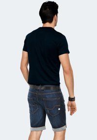 Marineblaues kurzärmliges Shirt mit Rundhalsausschnitt, kombiniert mit dunklen Denim-Shorts mit aufgerolltem Saum und kontrastierenden Nähten an den Gesäßtaschen.