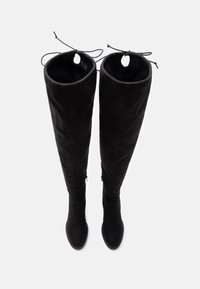 Melni uz ceļiem iedodami zābaki, kas izgatavoti no mīkstas zamšādas, ar noapaļotu purngali, paplašinātu augšdaļu un funkcionālām auklām augšā.