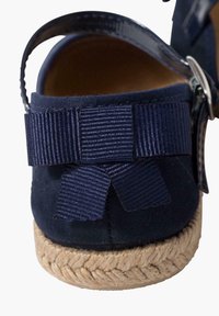 Navy suede espadrille heel with woven jute sole. Features a decorative navy ribbon bow and an adjustable ankle strap. Smooth texture.