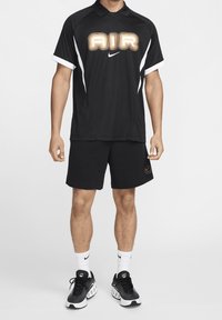 Svart atletisk polo med "AIR"-logotyp, vita accenter; kombinerad med svarta shorts och svarta sneakers med vita sulor och logotyp.