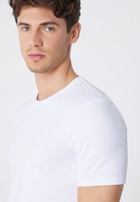 Weißes T-Shirt mit kurzen Ärmeln und Rundhalsausschnitt, aus einem glatten, leichten Material gefertigt. Verfügt über ein tailliertes Design, das sich dem Körper anpasst.