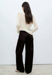 Pull en maille crème à manches longues avec un motif lâche et ouvert, associé à un pantalon noir taille haute à jambes larges. Texture lisse, design minimaliste.