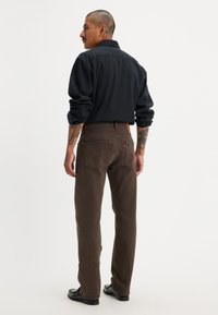 Pantalones de mezclilla marrones con un diseño de pierna recta, combinados con una camiseta de manga larga negra. Presentan bolsillos traseros y una etiqueta de cuero en la cintura.