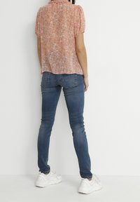 Pink floral blouse with short puff sleeves, ruffled neckline, paired with fitted dark blue jeans and white sneakers.