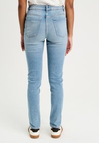Lysblå skinny jeans med mid-rise talje, to baglommer og en ren afslutning ved anklerne, parret med sort-hvide sneakers.