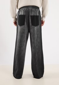 Schwarze weit geschnittene Hose mit einem verblassten grauen Muster. Verfügt über schwarze aufgesetzte Taschen auf der Rückseite. Elastischer Bund für Komfort.