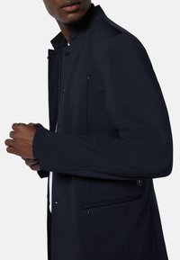 Marinblå jacka med ståkrage, med dragkedja och sidofickor, tillverkad av mjukt tyg med skräddarsydd passform och rena linjer.