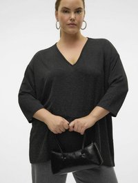 Haut noir texturé avec un décolleté en V et des manches trois-quarts, associé à un petit sac à main noir. Le mannequin tient le sac avec les deux mains.