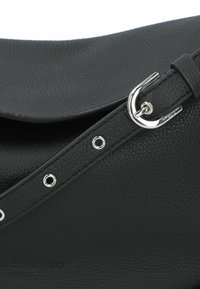Borsa a tracolla in pelle nera con superficie testurizzata, patta pieghevole, accessori in argento e occhielli circolari lungo la tracolla.