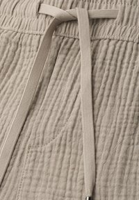 Tissu beige texturé avec taille élastique, poche latérale et cordon plat tissé noué d'un simple nœud.