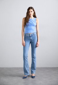 Light blue sleeveless top with ruching, paired with light blue flared jeans. Model wears blue pointed heels. Smooth fabric with a fitted design.