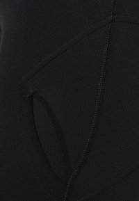 Schwarze Sportleggings mit glatter Textur, die über eine seitliche Tasche und geschwungene Nahtdetails verfügen. Der dehnbare Stoff verbessert Passform und Komfort.