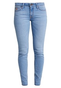 Jeans skinny de denim azul claro con cierre de botón, cinco bolsillos y un ligero desgaste. Presenta una etiqueta en el bolsillo trasero.