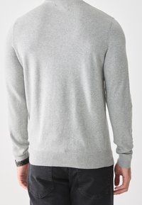 Grauer Strickpullover mit rundem Ausschnitt, langen Ärmeln und gerippten Bündchen sowie Saum. Glatte Textur, schlichtes Design, getragen mit dunkler Hose.